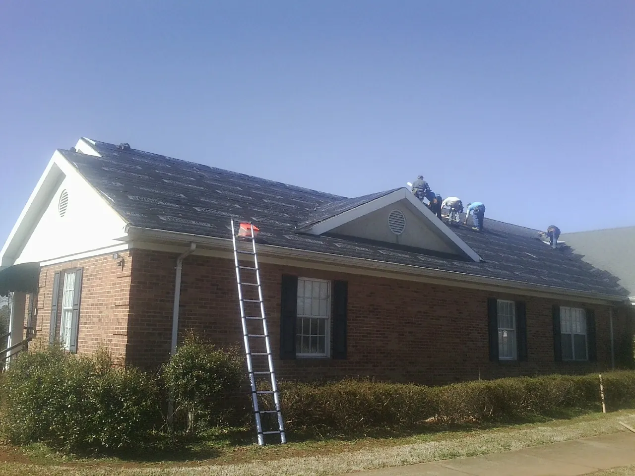 Crew tearing shingles off a brick ranch roof with a ladder set — Metal Roof Repair work by our crew in Good Hope